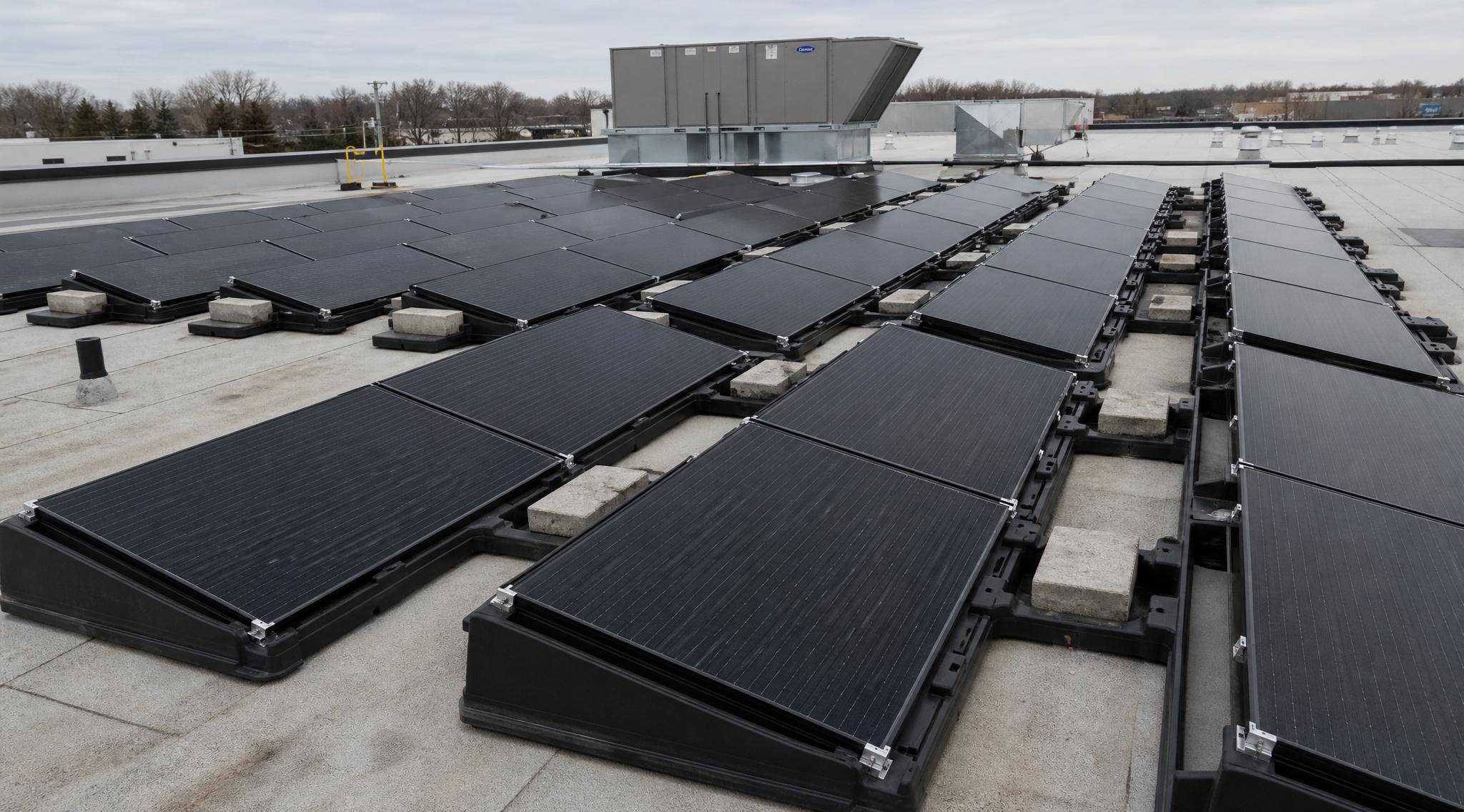 Wide view of a ballasted, non-penetrating PV array on a flat commercial roof, weighted with concrete blocks.