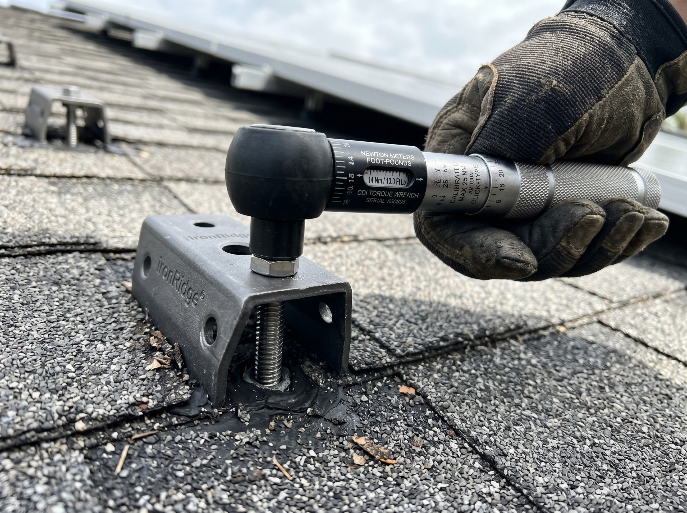 Calibrated torque wrench tightening a fastener on a roof-mounted PV foot on a composition-shingle roof.