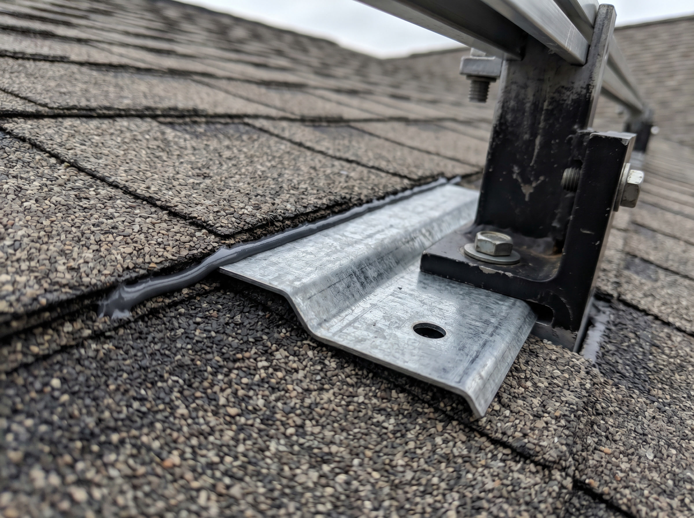 Metal step flashing slid under the upslope shingle course, with the mount and a sealant bead on top.